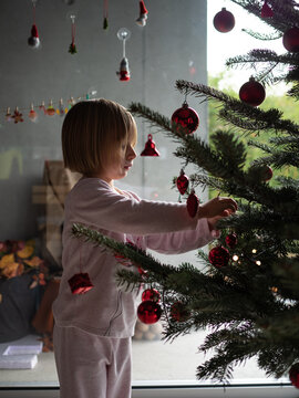 Winter holidays, charity and people concept. Happy little girl decorating christmas tree at home.