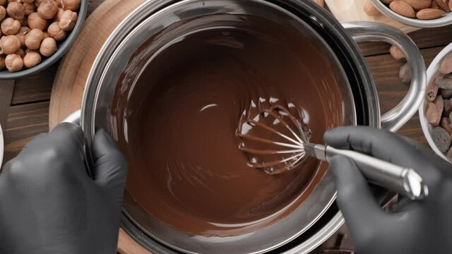 Confectioner stirring melted dark chocolate in a bowl, top view, close-up. Liquid hot chocolate. Confectionery preparation. Melted chocolate preparation