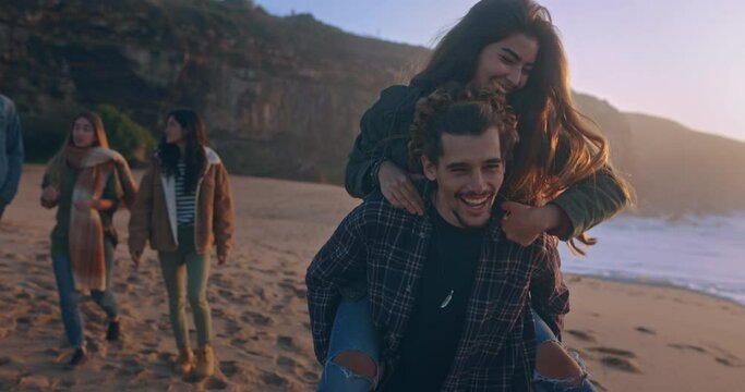 Young couple piggyback ride on the beach at sunset
