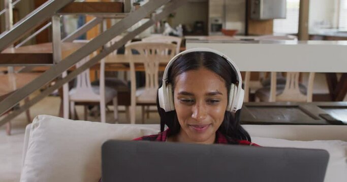 Mixed race woman on couch at home using laptop listening to music