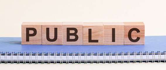 Public - a word made of wooden blocks with black letters, a row of blocks is located on a blue Notepad.