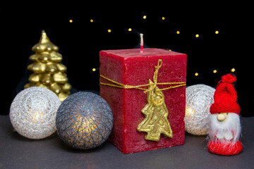 Christmas composition with big, red candle in the middle, surrounded by glowing and golden baubles and golden Christmas tree, black sparkling background.