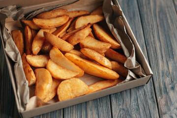 Slices of fried potatoes in box for food delivery. Delivered take away fast food on wooden background. Tasty fried potatoes from take away menu. Eco packaging. copy space. food delivery service