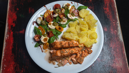Boiled potatoes, fresh salad and roasted salmon on white plate. Dark wooden background. Cuisine concept.