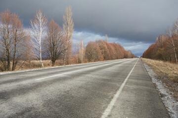 Empty winter highway without snow, with trees without leaves on the sides