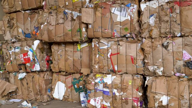 Close-up panning view of compressed and tied up blocks of cardboard awaiting recycling at a recycling plant