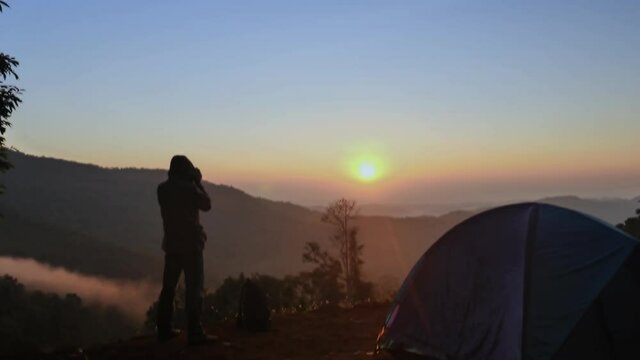 4k footage ; one man taking pictures of the beautiful of the rising sun on high hill, and a group of white fog moving along the lower tree line. amazing of Mea Tang, Chiang Mai, Thailand.