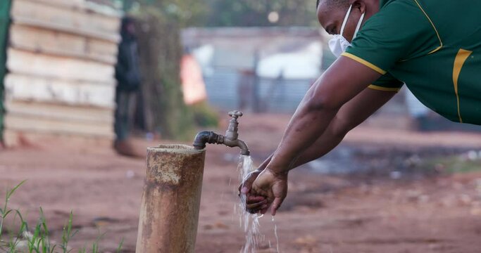 Black african man washing his hands at an outside tap in a squatter camp to prevent Covid-19 infection during Coronavirus pandemic