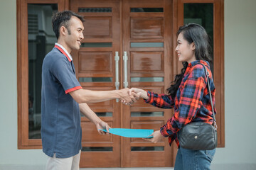 male housing developer handing home certificate to customer while shaking hands with new home background