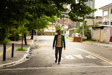 Homem elegante, usando &oacute;culos de sol e blazer, caminhando na rua.