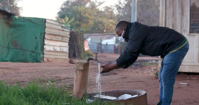 Black african man washing his hands at an outside tap in a squatter camp to prevent Covid-19 infection during Coronavirus pandemic