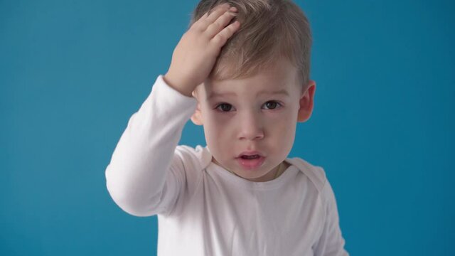 medicine, dermatology, treatment, inflammation, concepts - preschool minor toddler kid boy scratche his dandruff head, dry itchy face on blue background. Food allergies, urticaria, gluten intolerance