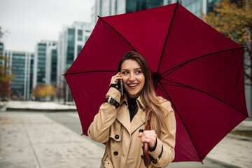 A beautiful young woman standing under an umbrella and talking on the phone