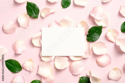 Blank paper card mockup with rose petals and green leaves on pink background. Flat lay, view from above. Greeting card template for Valentines Day, Mothers Day, birthday.