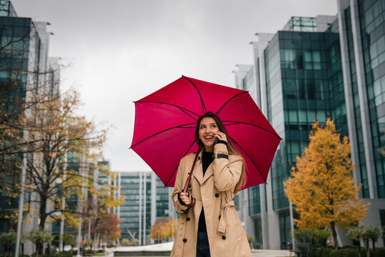 A beautiful young woman standing under an umbrella and talking on the phone - Powered by Adobe