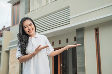 beautiful Asian woman stands with a hand gesture to offer something in front of the new house