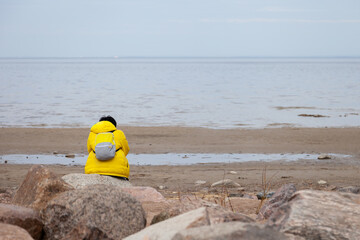 A lonely man in a yellow jacket sits on a stone alone and looks at the sea. Privacy concept in nature.
