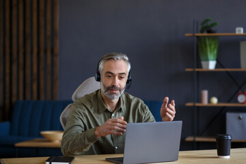 Portrait of grey-haired senior handsome man teaching online. Online education, remote working, home education. Online meeting, video call, video conference, courses online.