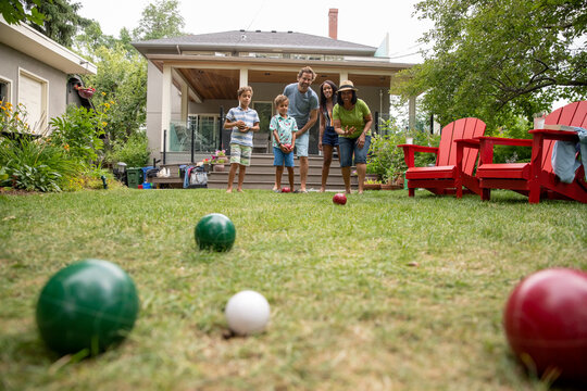 Family playing lawn bowl in backyard