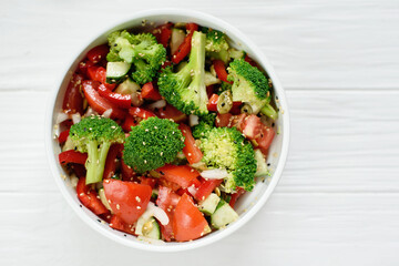 Vegetable salad. bowl of salad with fresh vegetables and greens, cucumber, tomatoes, red pepper, broccoli cabbage. and olive oil on white background. Top view. Healthy food.
