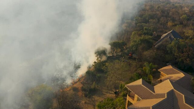 Climate emergency.Aerial close-up view of a grass fire burning very close to a housing estate in Southern Africa. Fire is caused by drought and climate change