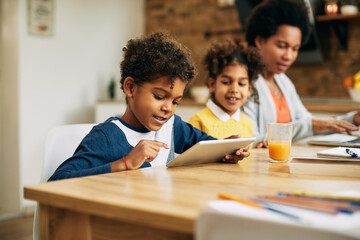 Small black boy surfing the net on digital tablet at home.
