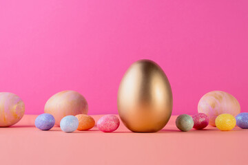 Trendy Easter background with Gold and colored Easter eggs on a light coral color background with copy space. Top view still life. Easter concept.