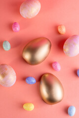Trendy Easter background with Gold and colored Easter eggs on a light coral color background with copy space. Top view still life. Easter concept.