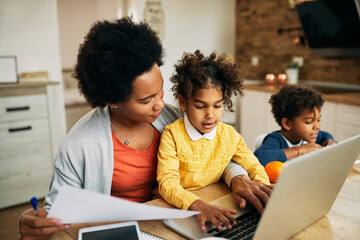 Black working mother and her daughter using laptop at home.