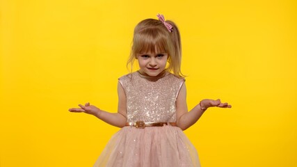 Irritated child girl in dress raising hands in questioning gesture why, what. Kid scolding with indignant expression, blaming in defeat. Yellow background studio. People emotions concept. Copy space