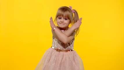 Little kid girl 5-6 years old in dress looking at camera crossed hands showing stop gesture. Posing isolated on yellow background studio. People emotions. Childhood lifestyle concept