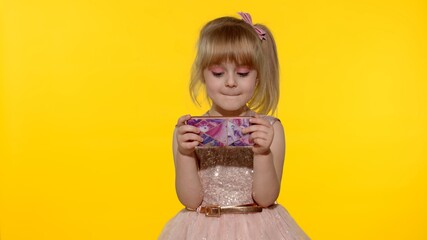 Little girl using smartphone. Portrait of child texting on smartphone. Kid enthusiastically playing games on mobile phone isolated on yellow background in studio. Technology for children