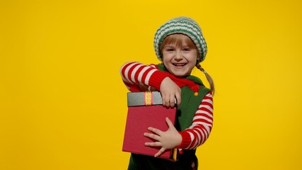 Teen kid girl in Christmas elf Santa helper costume on yellow background. Child getting present gift box, expressing amazement, extreme happiness looking inside box. New Year holidays celebration