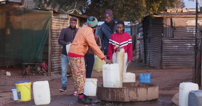 Poor Black African people getting water in containers from a communal tap in an informal settlement