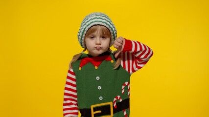 Displesed blonde kid teen girl in Christmas elf Santa helper costume doesnt agree with ideas how to celebrate New Year keeps thumbs down, dislike gesture