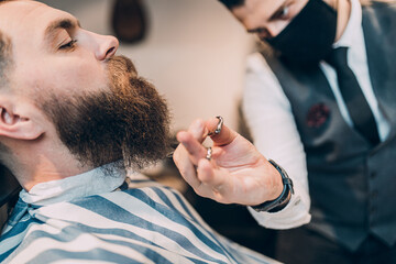 Fototapeta premium Young good looking hipste man visiting barber shop. Trendy and stylish beard styling and cut.