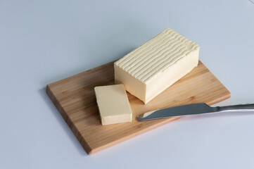 Wooden board with cut block of butter and knife on white background