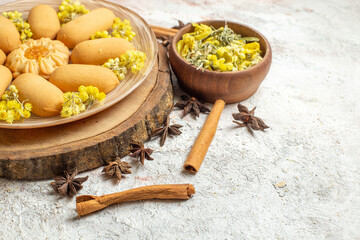 cinnamon sticks and a plate of tasty cookies and a bowl of dry flower and anise on marble ground