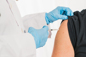 Putting a vaccine on a man's shoulder. Flu vaccine. Coronavirus vaccine. The female doctor vaccinated or syringe to injection to the young patient. Medical healthcare concept