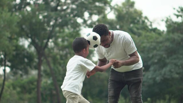Cheerful african american father and son playing with football in park, Happiness family concepts