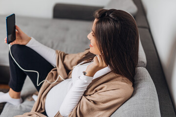 Beautiful young smiling pregnant woman sitting on sofa and  communicates via video chat.