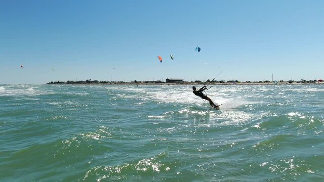 A man is kitesurfing near the seashore, more kite surfers in the background, 4k