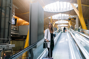 Young blonde woman on the walkway at the airport with luggage