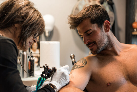 Focused woman making tattoo for smiling man