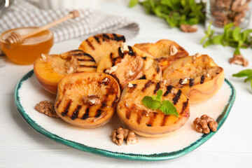 Delicious grilled peaches with mint and walnuts on white wooden table