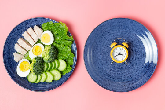 Food and alarm clock on pink background, intermittent fasting concept.