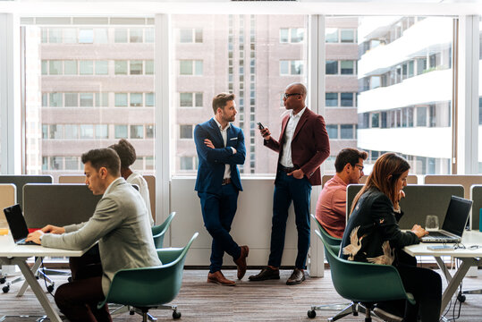 Business owners in formal suits chatting and browsing smartphone in busy office