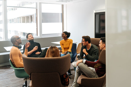 Contemporary group of coworkers in casual wear smiling while having conversation at office