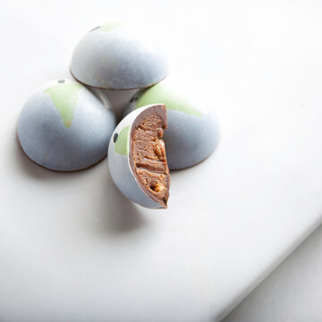 dome shaped chocolate candy bonbons stuffed with sesame praline. Decorated with a little christmas tree on white background. Exclusive handcrafted bonbon