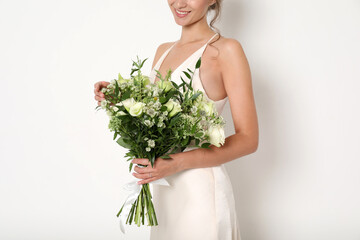 Young bride wearing wedding dress with beautiful bouquet on light background, closeup